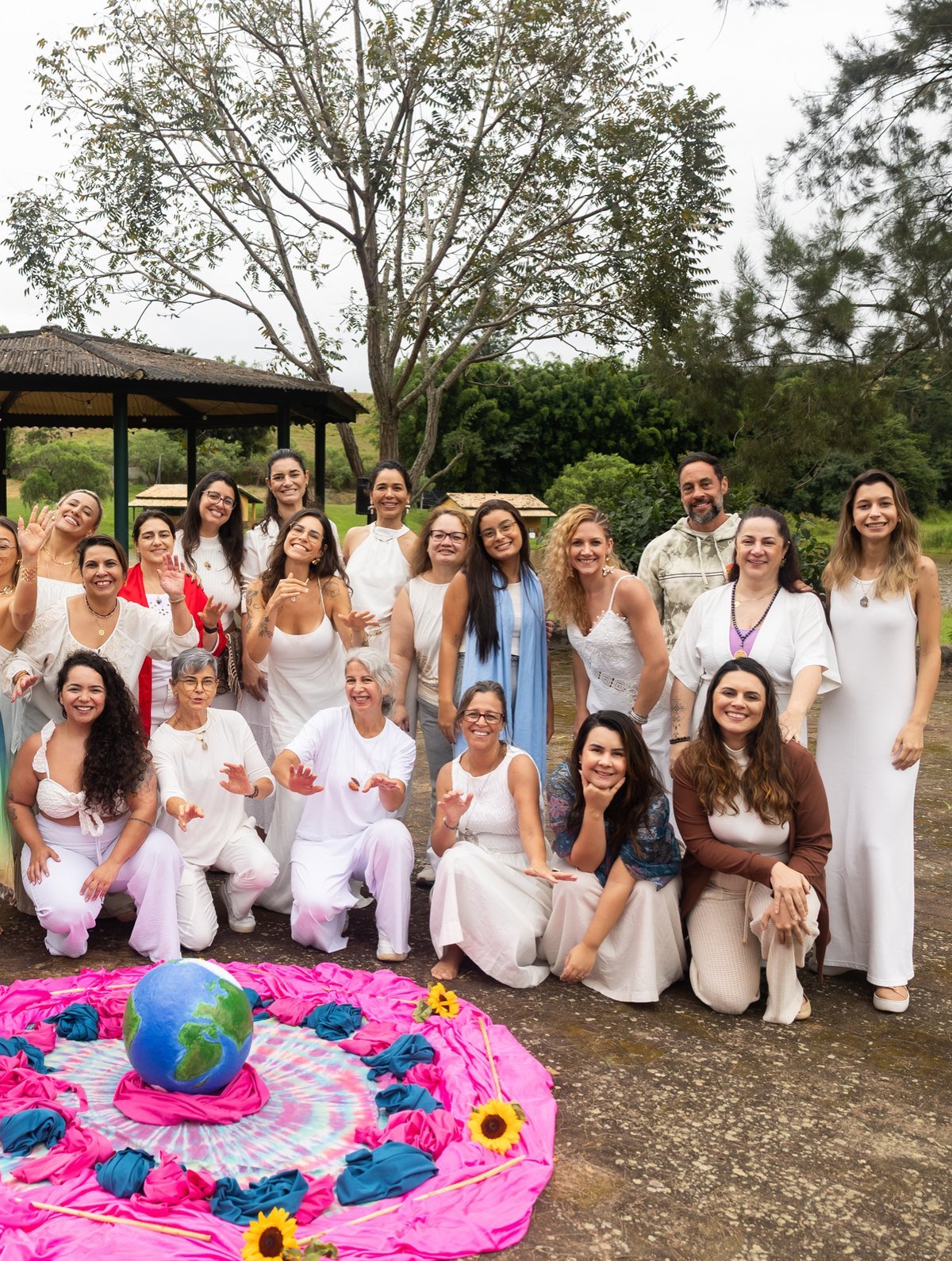 Grupo de mulheres vestidas de branco reunido em volta de uma mandala de flores